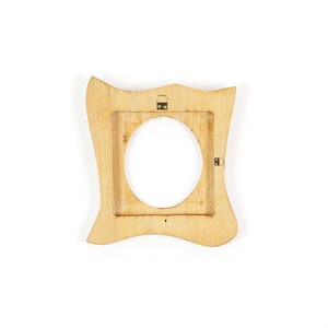 K&ouml;nnte beinhalten: Ein hellfarbiger Holzbilderrahmen mit einem einzigartigen, wellenf&ouml;rmigen Design. Der Rahmen hat eine kreisf&ouml;rmige &Ouml;ffnung in der Mitte und eine quadratische &Ouml;ffnung in der Mitte. Der Rahmen hat oben ein kleines Autosymbol.