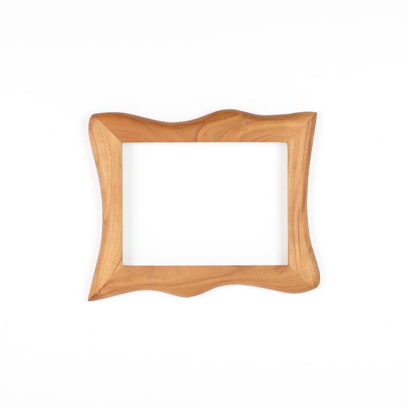 Op de afbeelding: Een lichtbruine houten fotolijst met een uniek, golvend ontwerp. De lijst heeft een rechthoekige opening en is gemaakt van lichtgekleurd hout. De lijst is leeg en klaar voor een foto of kunstwerk.