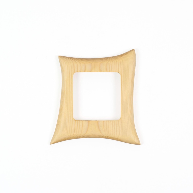 May include: A light-coloured wooden picture frame with a square central opening and four concave sides. The frame features a visible natural wood grain pattern throughout its surface, with smooth, curved edges that taper towards the corners.