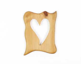 May include: A light brown wooden frame with a natural wood grain pattern and a smooth finish. The frame features an irregular, wavy outer edge and a central cutout shaped like a heart, showcasing the organic texture and knots of the wood.
