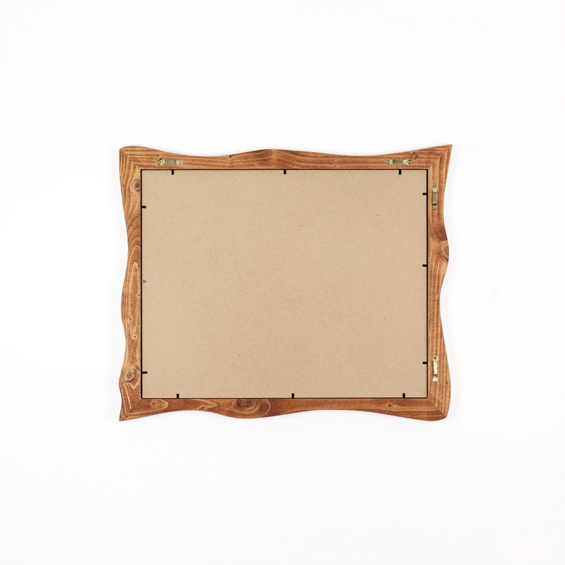 May include: A rectangular picture frame with a natural, wavy wooden edge and a light brown wood grain finish. The back of the frame is covered by a flat, tan-coloured backing board secured with small metal clips and includes two metal hanging hooks.