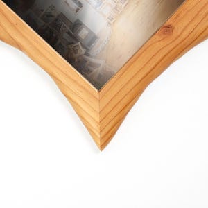 Pu&ograve; includere: Una cornice portafoto in legno marrone chiaro con un caratteristico design a forma di stella a cinque punte. La cornice presenta una texture naturale con venature del legno e una finitura liscia, circondando un vetro trasparente che mostra una foto.
