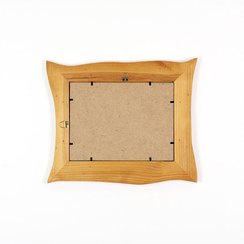May include: A wooden picture frame with a light brown, wavy edge. The back of the frame is visible, showing a cardboard backing and metal hanging hardware. The frame is set against a white background.