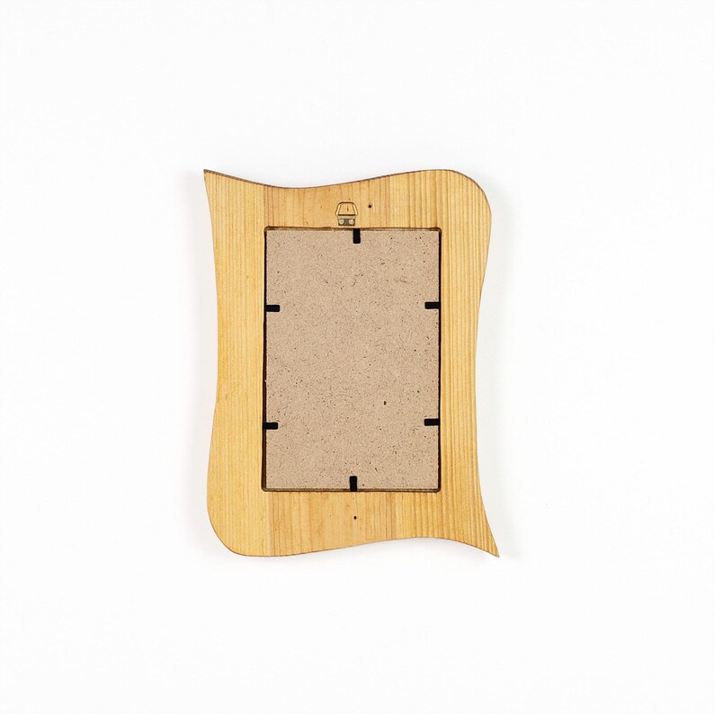 May include: A rectangular wooden picture frame with a wavy, curved outer edge. The frame features a light tan wood grain finish and a central rectangular backing board made of brown fibreboard, secured by six small black metal tabs.