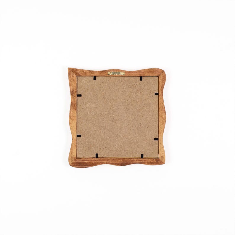 May include: A square wooden picture frame with a wavy, scalloped edge design. The back of the frame features a light brown fibreboard backing secured with eight small black metal clips and a central metal hanging bracket at the top edge.