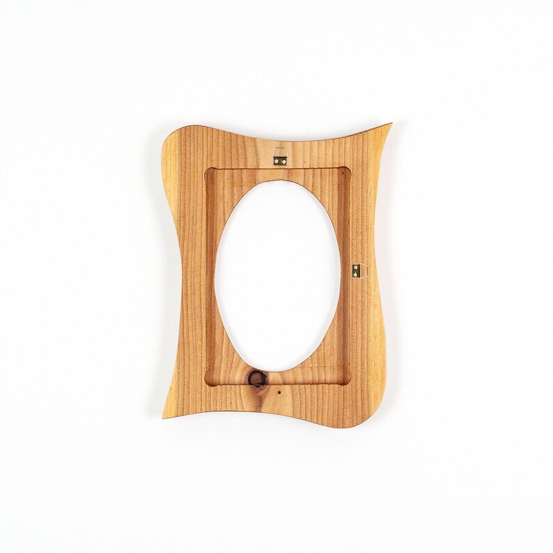 May include: A wooden picture frame with an oval opening. The frame is light brown with a wavy, organic shape. It has a natural wood grain texture and metal hanging hardware on the back.