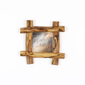 May include: A square picture frame constructed from four pieces of natural wood with a distinct grain pattern and dark, irregular streaks. The frame features a grid-like overlapping design at the corners, enclosing a central photograph of an interior space.