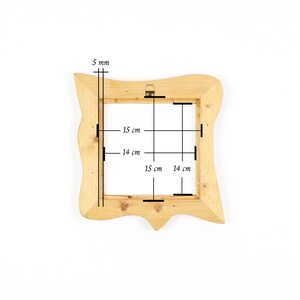 K&ouml;nnte beinhalten: Ein hellfarbener Holzrahmen mit unregelm&auml;&szlig;ig gewelltem Au&szlig;enrand und quadratischer Innen&ouml;ffnung. Der Rahmen weist technische Markierungen auf, die eine Dicke von 5 mm sowie Innenma&szlig;e von 15 cm mal 15 cm und 14 cm mal 14 cm angeben.