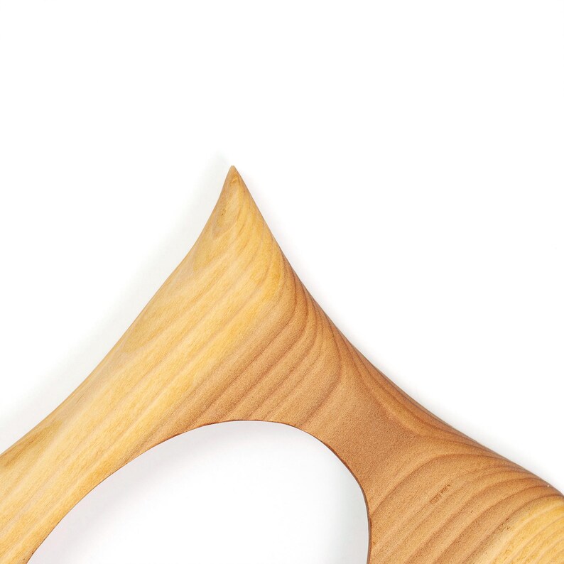 May include: Close-up of a wooden object with a light brown color and a smooth, curved design. The object has a pointed top and a circular opening. The wood grain is visible, adding texture to the piece. The object is set against a white background.