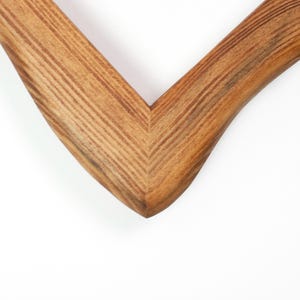May include: Close-up of a wooden picture frame corner. The frame is made of light brown wood with visible grain patterns. The corner is a sharp V-shape, with a smooth, curved outer edge.