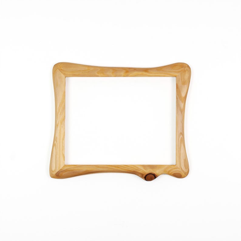 Op de afbeelding: Een lichtgekleurde houten fotolijst met een uniek, gebogen ontwerp. De lijst heeft een natuurlijke houtnerf en een knoopdetail in de rechter benedenhoek. De lijst is leeg, met een witte achtergrond.