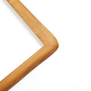 Pu&ograve; includere: Un appendiabiti in legno con finitura naturale. L'appendiabiti ha una forma rettangolare con angoli arrotondati e un gancio nella parte superiore. La venatura del legno &egrave; visibile e l'appendiabiti &egrave; posto su uno sfondo bianco.