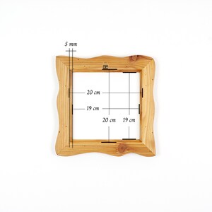 Puede incluir: Un marco de fotos cuadrado de madera con un acabado de veta de madera marr&oacute;n claro natural y bordes exteriores ondulados. El marco cuenta con un soporte met&aacute;lico para colgar en la parte superior central. Las marcas t&eacute;cnicas indican 5 mm de grosor, 20 cm de alto y 19 cm de ancho.