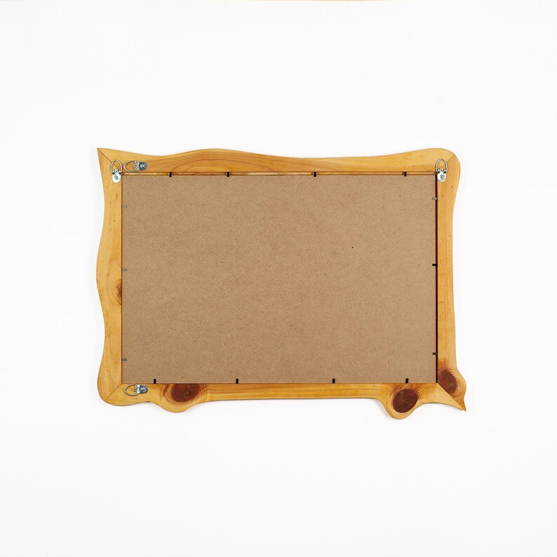 May include: A rectangular wooden picture frame with a natural light brown finish and visible wood grain knots. The back of the frame is covered by a flat brown fiberboard panel secured with metal clips and includes two metal D-ring hangers.