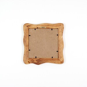 K&ouml;nnte beinhalten: Ein quadratischer Bilderrahmen aus Holz mit einem wellenf&ouml;rmigen Rand. Der Rahmen besteht aus hellbraunem Holz und hat eine Kartonr&uuml;ckwand. Die R&uuml;ckseite des Rahmens hat schwarze Laschen, um ein Bild zu halten.
