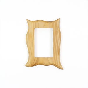 May include: A rectangular picture frame crafted from light-colored wood with a visible natural grain pattern. The frame features a distinctively wavy, undulating outer edge on all four sides, surrounding a central rectangular opening.