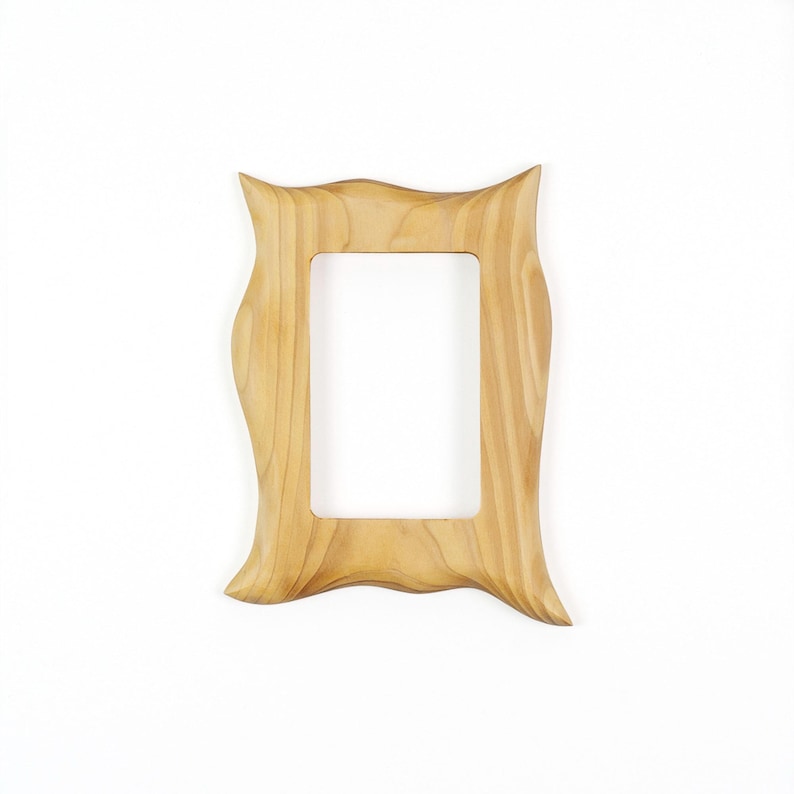 May include: A rectangular picture frame crafted from light-colored wood with a visible natural grain pattern. The frame features a distinctively wavy, undulating outer edge on all four sides, surrounding a central rectangular opening.