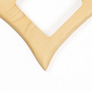 May include: A light-coloured wooden frame with a distinct V-shaped corner. The natural grain of the wood is visible throughout the surface, showing a smooth texture and a pointed angle where two straight edges meet to form a sharp, clean point.