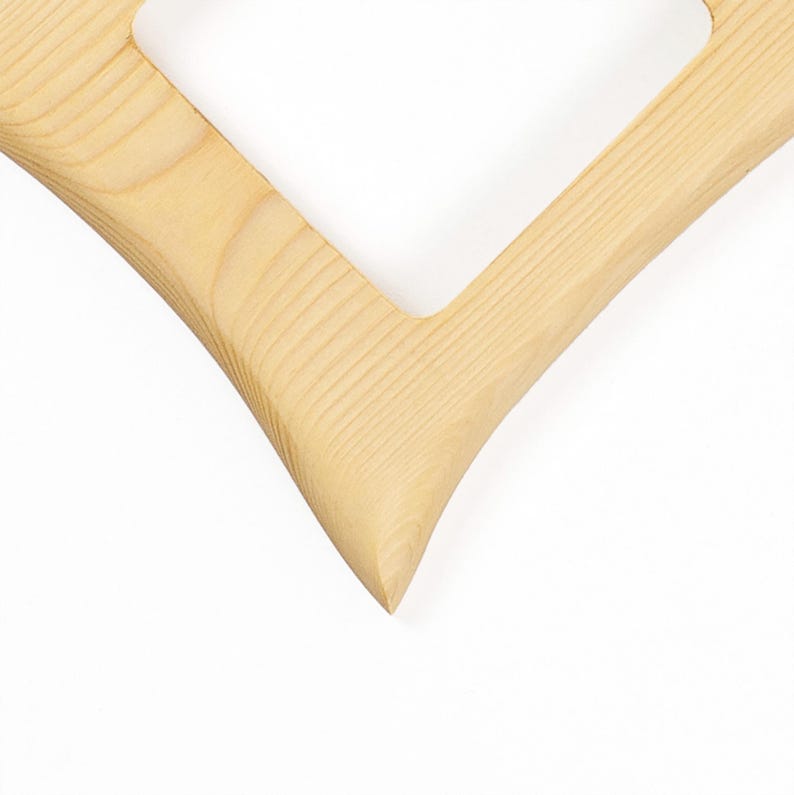 May include: A light-coloured wooden frame with a distinct V-shaped corner. The natural grain of the wood is visible throughout the surface, showing a smooth texture and a pointed angle where two straight edges meet to form a sharp, clean point.