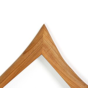 Puede incluir: Una percha de madera en forma de V con un acabado de grano de madera natural de color marr&oacute;n claro. Los dos brazos de la percha se unen en un v&eacute;rtice afilado y puntiagudo, mostrando una construcci&oacute;n de junta a inglete sin costuras.