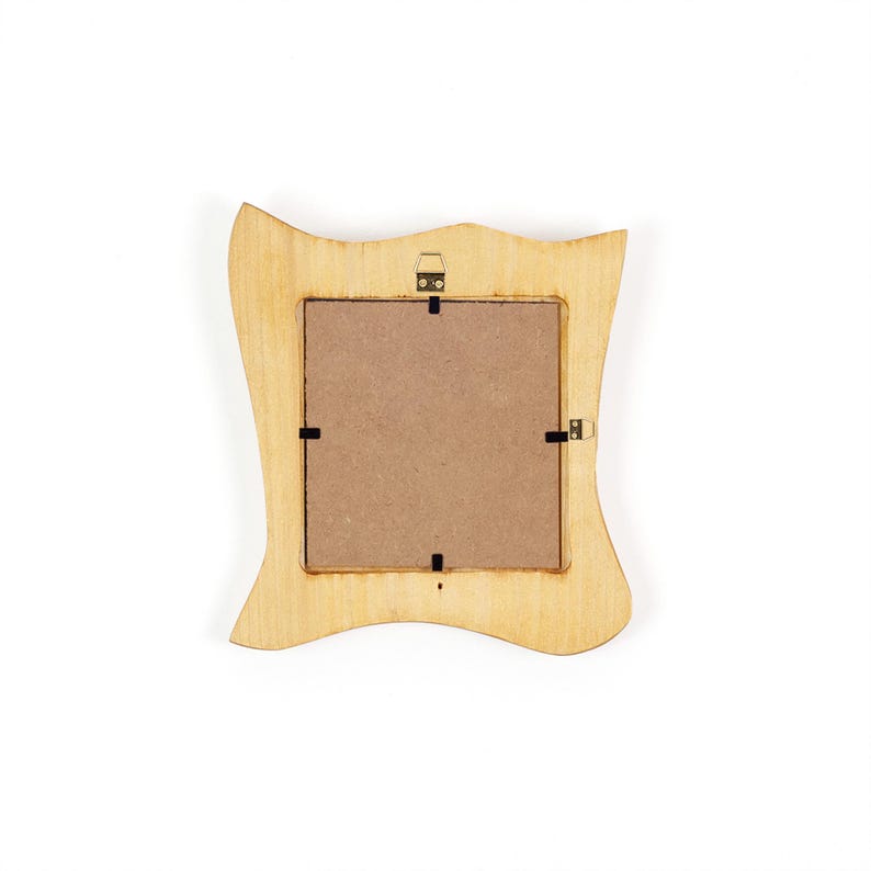 K&ouml;nnte beinhalten: R&uuml;ckseite eines hellfarbenen Holzfotorahmens mit einem einzigartigen, wellenf&ouml;rmigen Design. Der Rahmen hat eine quadratische &Ouml;ffnung mit brauner R&uuml;ckseite und schwarzen Clips. Oben befindet sich eine kleine Metallaufh&auml;ngung zur Wandmontage.