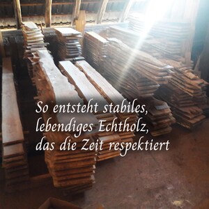 May include: Stacks of raw, unfinished wooden planks in a workshop setting. The planks vary in size and shape, with visible wood grain. Text in the image reads: "So entsteht stabiles, lebendiges Echtholz, das die Zeit respektiert."