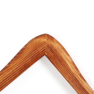 May include: Close-up of a wooden picture frame corner. The frame is made of light brown wood with visible grain and a smooth, curved corner. The frame is set against a white background.