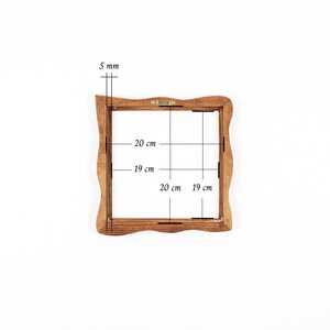 May include: A square wooden frame with wavy edges and a brown finish. The frame features a metal hanging bracket on the top edge. Technical annotations indicate a thickness of 5 mm, with internal dimensions of 19 cm by 19 cm and external dimensions of 20 cm by 20 cm.