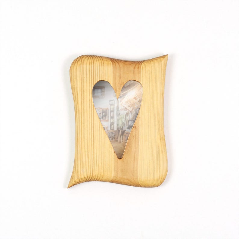 May include: A light brown wooden picture frame with a natural wood grain pattern. The frame features a distinct wavy, organic shape with a central heart-shaped cutout for displaying a photograph. The wood has a smooth, polished finish throughout.