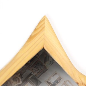 May include: A light-colored wooden picture frame with a unique, pointed top corner. The frame has a natural wood grain finish and a curved edge. The glass reflects images of other framed pictures.
