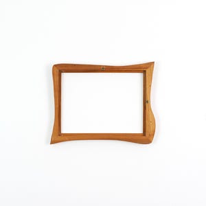 May include: A rectangular wooden picture frame featuring an organic, wavy edge design. The frame is crafted from light brown wood with a visible grain pattern and includes small metal mounting hardware attached to the inner side of the frame.