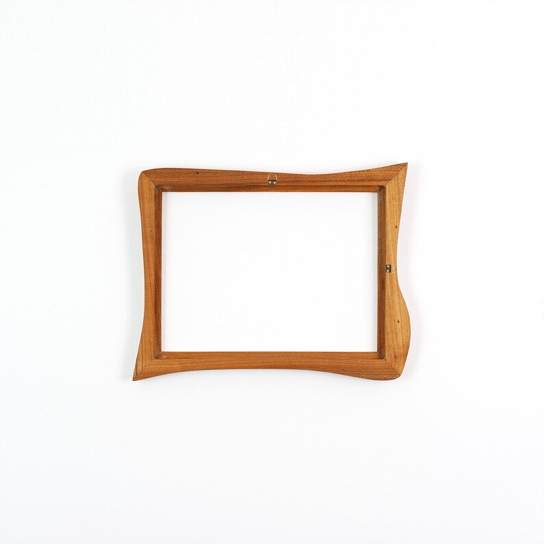 May include: A rectangular wooden picture frame featuring an organic, wavy edge design. The frame is crafted from light brown wood with a visible grain pattern and includes small metal mounting hardware attached to the inner side of the frame.