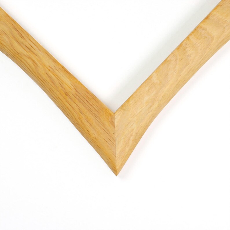 May include: A corner section of a light brown wooden picture frame featuring a visible natural wood grain pattern. The frame is constructed with a mitered joint that forms a sharp V-shaped angle, showcasing the smooth texture and light tan color of the wood.