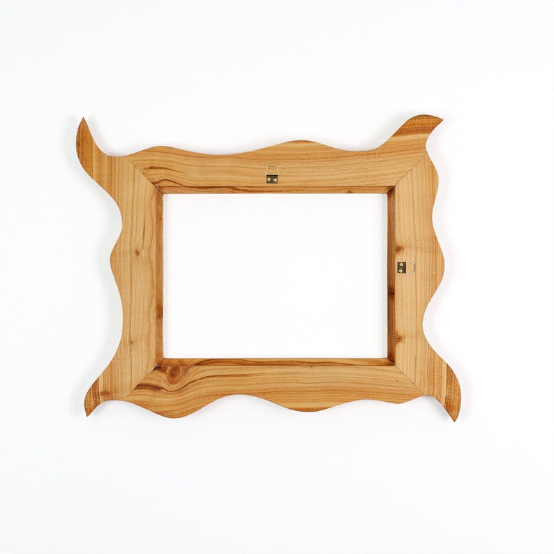 Puede incluir: Un marco de fotos rectangular de madera con una veta natural de color marr&oacute;n claro y un borde exterior ondulado e irregular. El marco incluye dos peque&ntilde;os soportes de montaje de metal fijados en el lado interior para colgar.