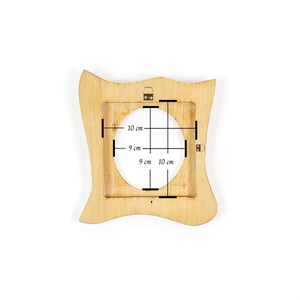 K&ouml;nnte beinhalten: Ein hellfarbiger Holzbilderrahmen mit quadratischer &Ouml;ffnung und wellenf&ouml;rmigen Kanten. Die &Ouml;ffnung misst 9 cm x 10 cm. Der Rahmen hat einen kleinen Aufh&auml;ngemechanismus auf der R&uuml;ckseite.