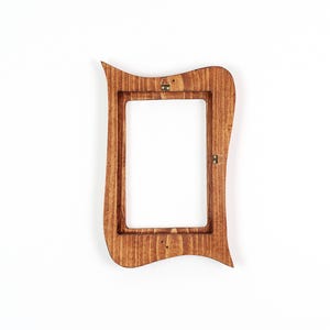 May include: A wooden picture frame with a distinctive, curved design. The frame is stained a warm brown colour and has a rectangular opening. Metal hardware is attached for hanging.