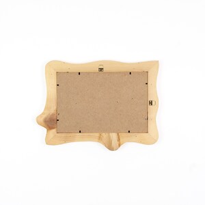 Puede incluir: Un marco de fotos rectangular hecho de madera natural de color claro con un perfil de borde irregular y org&aacute;nico. La parte posterior del marco cuenta con un panel de fibra marr&oacute;n asegurado con clips met&aacute;licos e incluye un soporte de metal.