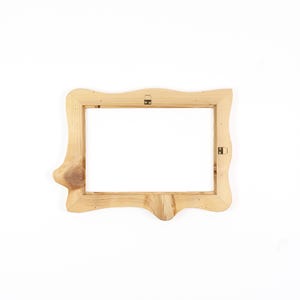 Puede incluir: Un marco de fotos rectangular de madera con un acabado natural marr&oacute;n claro y veta de madera visible. El marco presenta un borde exterior org&aacute;nico e irregular con un nudo prominente en el lado izquierdo y dos soportes met&aacute;licos para colgar.