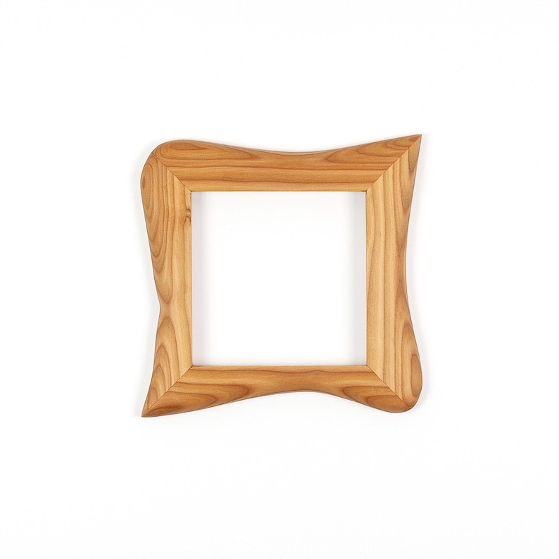 K&ouml;nnte beinhalten: Ein quadratischer Holzbilderrahmen mit hellbraunem Finish. Der Rahmen hat ein einzigartiges, wellenf&ouml;rmiges Design an den Au&szlig;enkanten. Der Rahmen ist leer, mit einem wei&szlig;en Hintergrund, der durch die Mitte sichtbar ist.
