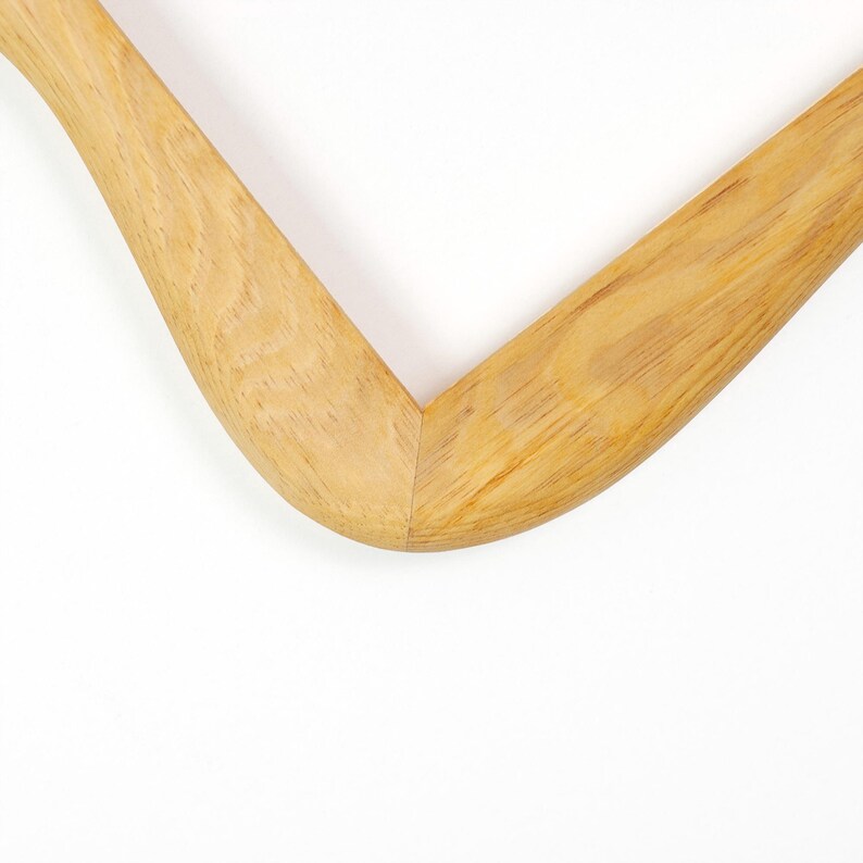 May include: A light brown wooden clothes hanger featuring a smooth, curved V-shaped design. The natural wood grain is clearly visible across the surface of the hanger, showcasing the texture and light tan color of the material in a close-up view.
