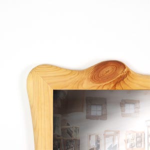 K&ouml;nnte beinhalten: Ein hellfarbiger Holzbilderrahmen mit nat&uuml;rlicher Holzmaserung. Der Rahmen hat eine einzigartige, geschwungene Oberseite und eine rechteckige &Ouml;ffnung f&uuml;r ein Foto oder Kunstwerk. Das Holz hat ein Knotendetail.