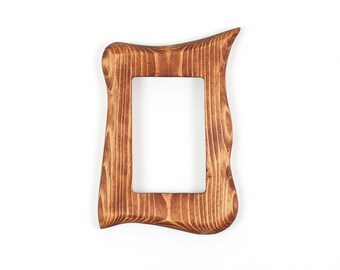 Op de afbeelding: Een rechthoekige houten fotolijst met een natuurlijke bruine houtnerfafwerking. De lijst heeft een onregelmatig, golvend en organisch ontwerp aan de buitenrand met een glad, gepolijst oppervlak rondom een centrale opening.