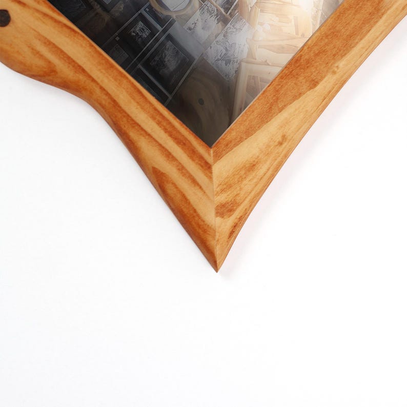 K&ouml;nnte beinhalten: Ein Bilderrahmen aus Holz mit einer nat&uuml;rlichen hellbraunen Holzmaserung und einer spitzen Ecke. Der Rahmen verf&uuml;gt &uuml;ber eine klare Glasscheibe, die eine Sammlung von schwarz-wei&szlig;en Fotografien bedeckt, die in einem Rastermuster angeordnet sind.