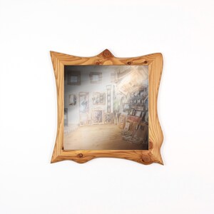May include: A square wooden mirror with a natural wood grain finish. The frame has a unique, wavy design. The mirror reflects a room filled with framed artwork, creating a gallery-like effect. The wood has a warm, light brown color.