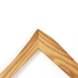 May include: A corner section of a wooden picture frame featuring a light brown natural wood grain pattern. The frame has a smooth, angled surface with a mitered joint at the top peak, showcasing the organic texture and warm tones of the wood.