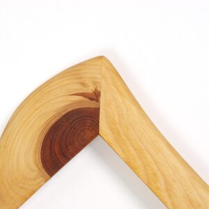Puede incluir: Una secci&oacute;n de esquina de un marco de madera con una uni&oacute;n a inglete. La madera muestra un patr&oacute;n de veta de color tostado claro con un detalle de nudo circular prominente de color marr&oacute;n rojizo oscuro en el lado izquierdo.