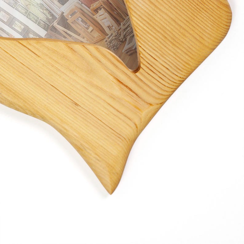 May include: A light-colored wooden picture frame with a unique, curved design. The frame has a natural wood grain texture and a smooth finish. The frame is partially visible, with a glimpse of the image it holds.