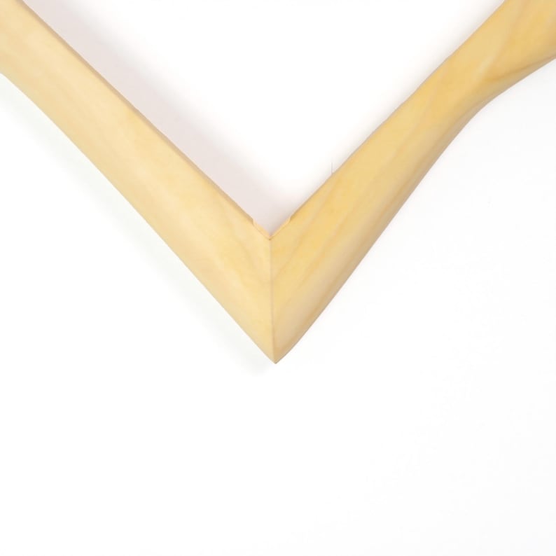 May include: A corner section of a light-coloured wooden picture frame. The frame features a smooth, natural wood grain finish with a clean mitred joint at the corner, forming a sharp V-shape. The wood has a pale, warm beige tone throughout.