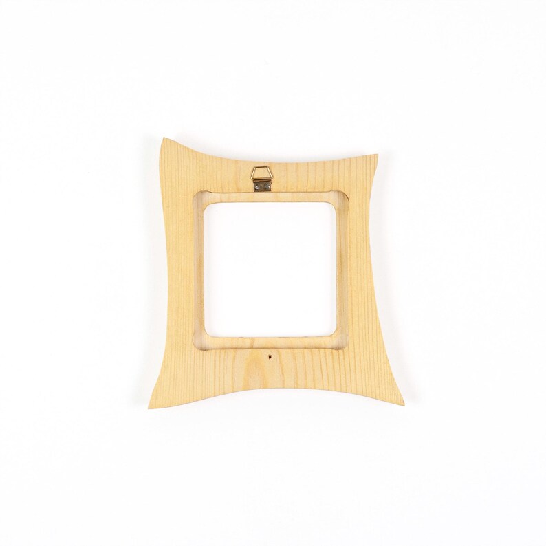 May include: A light-coloured wooden picture frame with a square central opening and curved, concave outer edges. The frame features a visible natural wood grain pattern and includes a small, centred metal hanging bracket on the top edge.