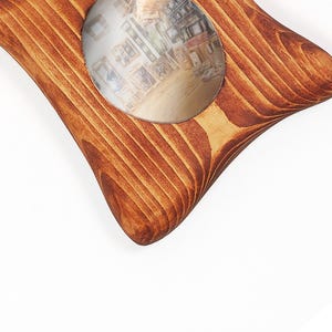 May include: A star-shaped wooden picture frame with a natural brown wood grain finish. The frame features a circular opening in the center that displays a photograph of various other picture frames arranged on a light-colored wooden floor surface.